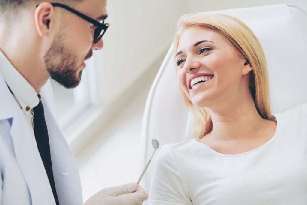 Male Dentist examining a female patients teeth with a mirror