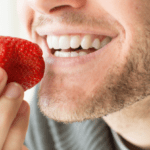 Young man holding a strawberry and smiling