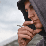 boy with black hoodie is smoking cigarette outdoor