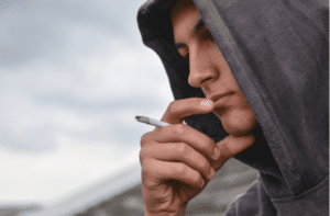 boy with black hoodie is smoking cigarette outdoor