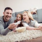 Father,mother and daughter lying on floor,watching TV and eating popcorn.