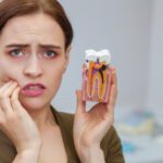 woman suffering from toothache, looking to the camera in despair, holding tooth mold showing cavity