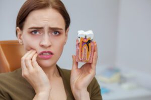 woman suffering from toothache, looking to the camera in despair, holding tooth mold showing cavity