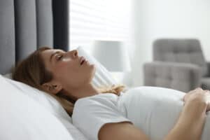 A woman lying on her back and snoring because of sleep apnea